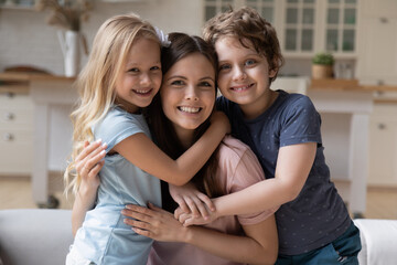 portrait of happy young mother hug cuddle with smiling little children relax on weekend at home, smi