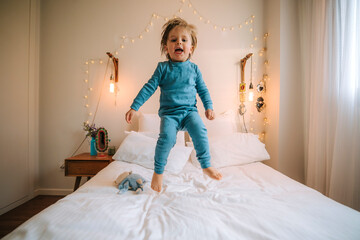 little blond boy has fun jumping and playing on a big bed. fun at home family at home