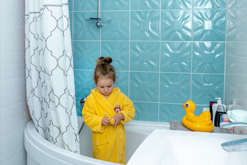 Little cute baby girl wears a yellow bathrobe in bathroom toilet room. Image with selective focus.