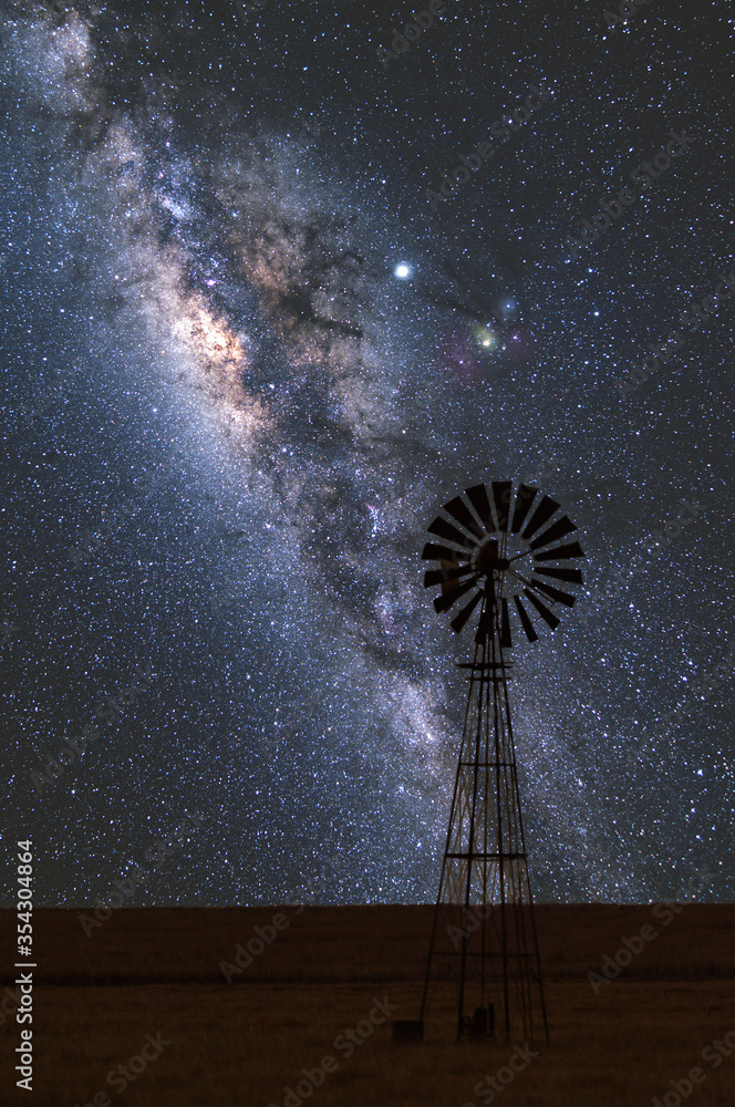 Wiatrak na farmie i nocne niebo gwiezdziste z centrum Drogi Mlecznej w bezksiężycową noc - obrazy, fototapety, plakaty 