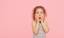 Portrait Of Surprised Cute Little Toddler Girl Child Over Pink Background. Looking At Camera. Points Hands To The Left Side. Advertising Childrens Products