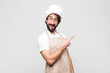 young crazy chef looking excited and surprised pointing to the side and upwards to copy space against white wall