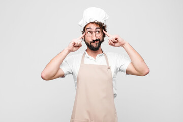 Wall Mural - young crazy chef looking concentrated and thinking hard on an idea, imagining a solution to a challenge or problem against white wall