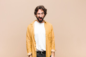 Wall Mural - young crazy cool man looking shocked, angry, annoyed or disappointed, open mouthed and furious against flat wall