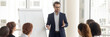 © fizkes - Speaker talking to audience makes presentation using flip chart interacts with group of staff employees, corporate seminar, training activity concept. Horizontal photo banner for website header design