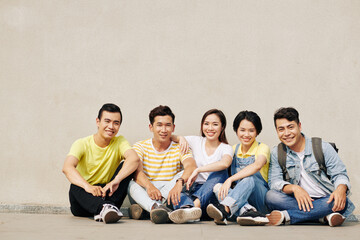 Canvas Print - Group of cheerful students sitting on ground next to and smiling at camera