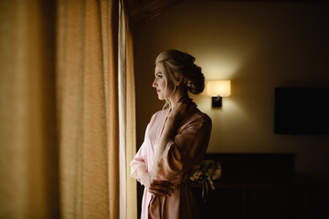 Poster - Beautiful blonde girl in a pink bathrobe looks out the window. Close-up.