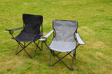 Two Grey And Black Empty Folding Camping Chairs In Green Lawn Grass Outdoors In Sunny Summer Day. Camping Equipment.
