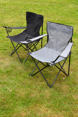 Two grey and black empty folding camping chairs in green lawn grass outdoors in sunny summer day. Camping equipment.
