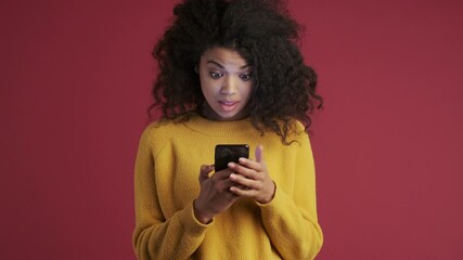 Young african surprised emotional pleased woman isolated over dark red burgundy background showing display of mobile phone