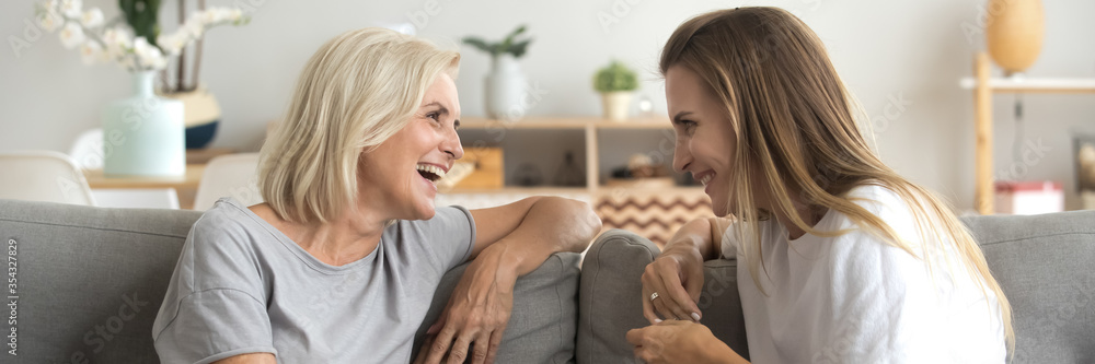 Grown up adult daughter middle-aged 60s mother seated on sofa having fun, two women gossiping enjoy positive conversation spend time together at home. Horizontal photo banner for website header design - obrazy, fototapety, plakaty 