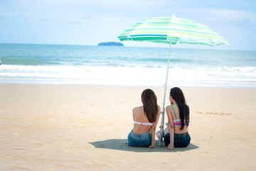 Happy summer holiday vacation, hot sexy beautiful two women in bikini setting under beach umbrella, resting and spending time to relexation on tropical island beach