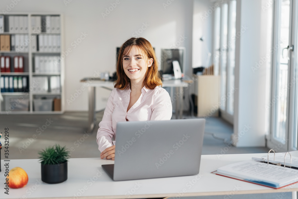 Smiling young friendly businesswoman at her desk - obrazy, fototapety, plakaty 