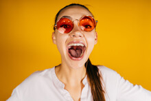 Cheers Cheers !! Girl Screams With Her Mouth Wide Open And Looking Through Pink Glasses On A Yellow Background