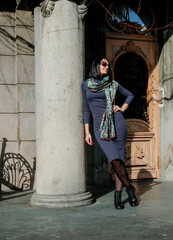 Wall Mural - Fashion, brunette woman in a dress and scarf in the street. Enjoys a sunny spring day. Girl model posing in Batumi, Georgia. Old city at background.