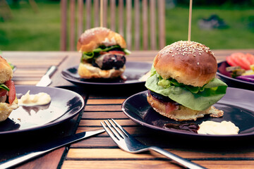 Homemade buger with meat and lettuce on a table in garden in picnic and barbecue outdoors. Healthy food on a plate in summer time. Close up. 