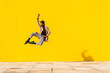 © VISTA by Westend61 - Young man dancing in front of yellow wall, jumping mid air