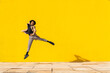 © VISTA by Westend61 - Young man dancing in front of yellow wall, jumping mid air