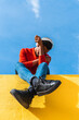© VISTA by Westend61 - Young man with headphones, sitting on yellow wall, listening music