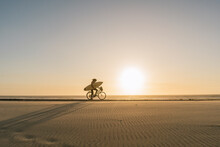 Surfer Riding A Bicycle During The Sunset In The Beach, Costa Nova, Portugal