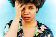 © VISTA by Westend61 - Portrait of Afro-American woman, hand on forehead, blue wall in the background