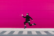 © VISTA by Westend61 - Young man listening to music and jumping in front of a pink wall
