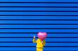 © VISTA by Westend61 - Little girl standing in front of blue background hiding behind pink balloon and showing victory sign