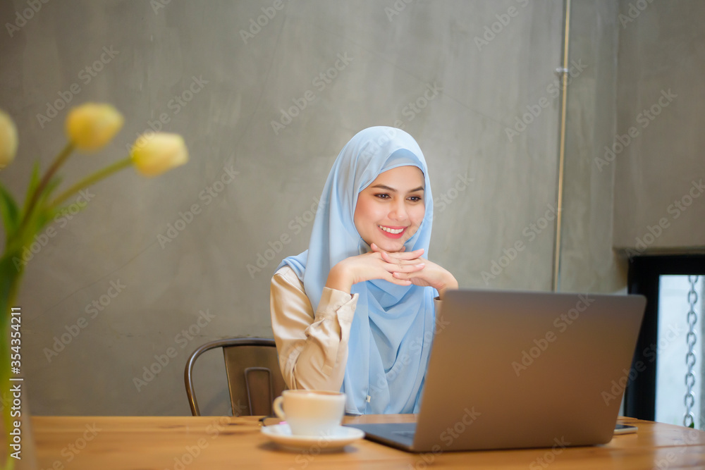 Muslim woman with hijab is working with laptop computer in coffee shop ...