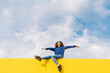 © VISTA by Westend61 - Happy young woman sitting on yellow wall against cloudy sky looking up