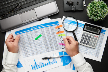 Top view of businessman's hands working with financial reports. Modern black office desk with laptop, notebook, pencil and a lot of things. Flat lay table layout.