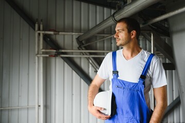 Wall Mural - Smiling and happy employee. Industrial worker indoors in factory. Young technician with white hard hat.