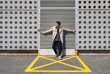 Mid Adult Man Standing In Yellow Marked Area In Front Of Concrete Wall, With Arms Outstretched