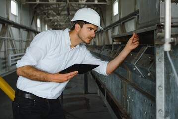 Wall Mural - Close up of young Caucasian smiling worker with helmet on head using tablet for work while standing in warehouse.