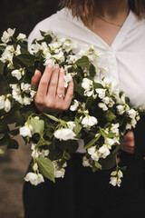 A girl in a white shirt holds a bouquet of flowers, an engagement ring on her hand, closeup photo. French manicure on hand
