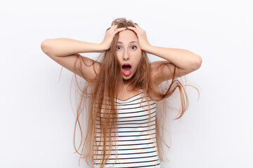 Wall Mural - yound blonde woman feeling horrified and shocked, raising hands to head and panicking at a mistake against white wall