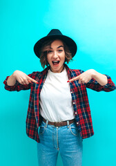 Wall Mural - Fashion portrait of young stylish hipster girl, wearing plaid shirt, white blank t-shirt and blue denim jeans isolated on blue studio wall. Mockup for print