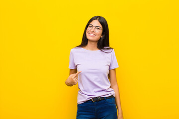 young pretty latin woman looking proud, confident and happy, smiling and pointing to self or making number one sign against flat wall