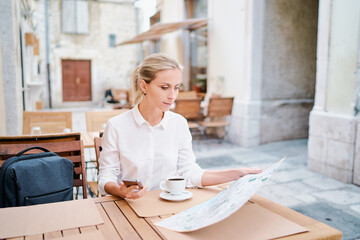 Wall Mural - Happy tourist drinking coffee. Pretty young woman with map sitting at table at old town cafe, outside. Travel by Europe.