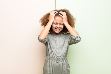 Wall Mural - african american little girl feeling stressed and anxious, depressed and frustrated with a headache, raising both hands to head against flat wall