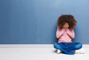 Sticker - african american little girl feeling sad, frustrated, nervous and depressed, covering face with both hands, crying sitting on the floor