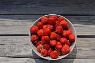 
ripe juicy strawberry berry in a plate on a wooden background under the sun