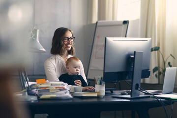 Business woman and mom is happy to be able to bring her baby with her to the office. Working on the computer. 