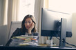 © Martin Villadsen - Unhappy business woman is tired of her job. Sitting infront of her computer with a large pile of paperwork on her desk.