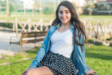 natural beautiful caucasian girl looking at the camera sitting on a wodden bench in the park.