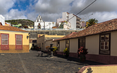 two yellow mediterranean buildings in the foreground with a fountain and a bench in front of them. a