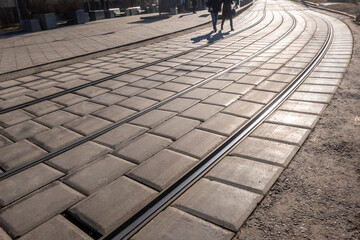 Tram ways in the city. 2 people are crossing the ways on sunny day. Background image.