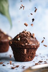 Poster - Vertical selective focus shot of chocolate cupcakes on a blue surface with chocolate chips falling