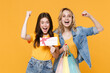© ViDi Studio - Surprised young women girls friends in denim clothes isolated on yellow background. People lifestyle concept. Hold package bag with purchases after shopping, gift certificate, doing winner gesture.