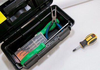 Screwdrivers and pliers lie in the gray open tool box, next to it lies a screwdriver