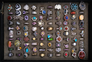 Assorted colorful vintage rings on a flea market stall sale in Italy, various designs and materials including precious stones, diamonds, silver, copper, gold and more, framed by a black velvet box